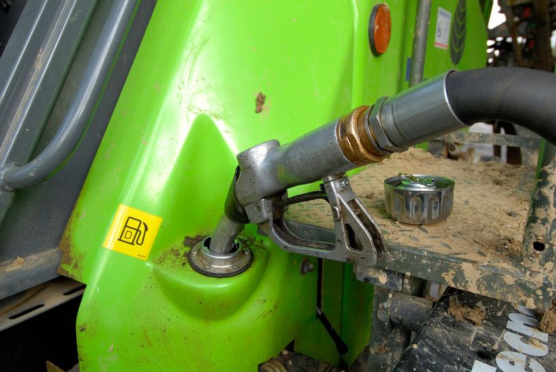 Un pistolet de remplissage de carburant est inséré dans l'orifice d'entrée du réservoir d'un véhicule agricole vert vif.