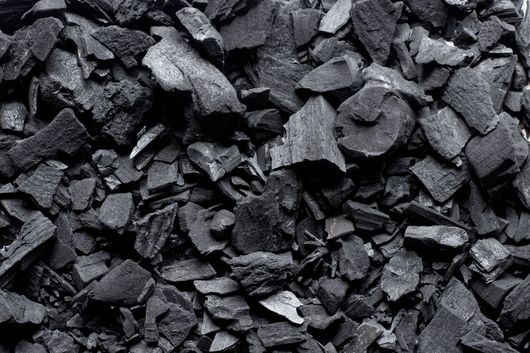 Gros plan sur de nombreux morceaux irréguliers et dentelés de charbon de bois noir empilés les uns sur les autres.