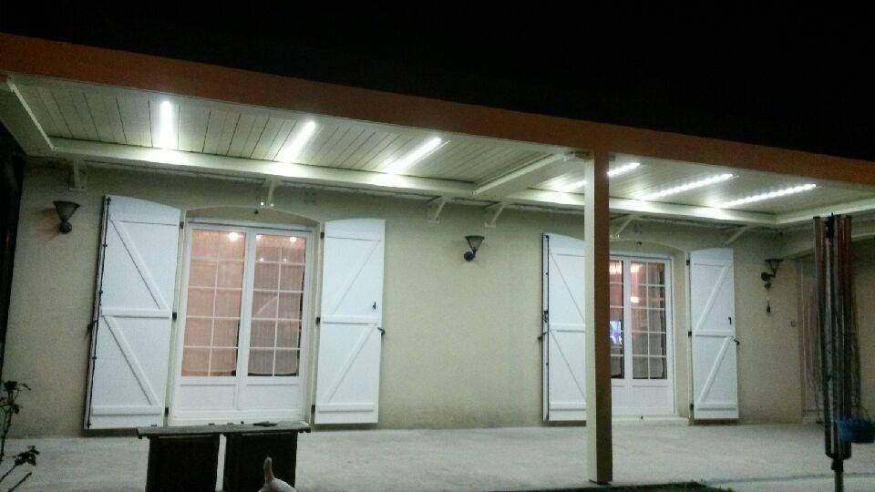 Deux portes-fenêtres blanches avec volets blancs sous une pergola éclairée