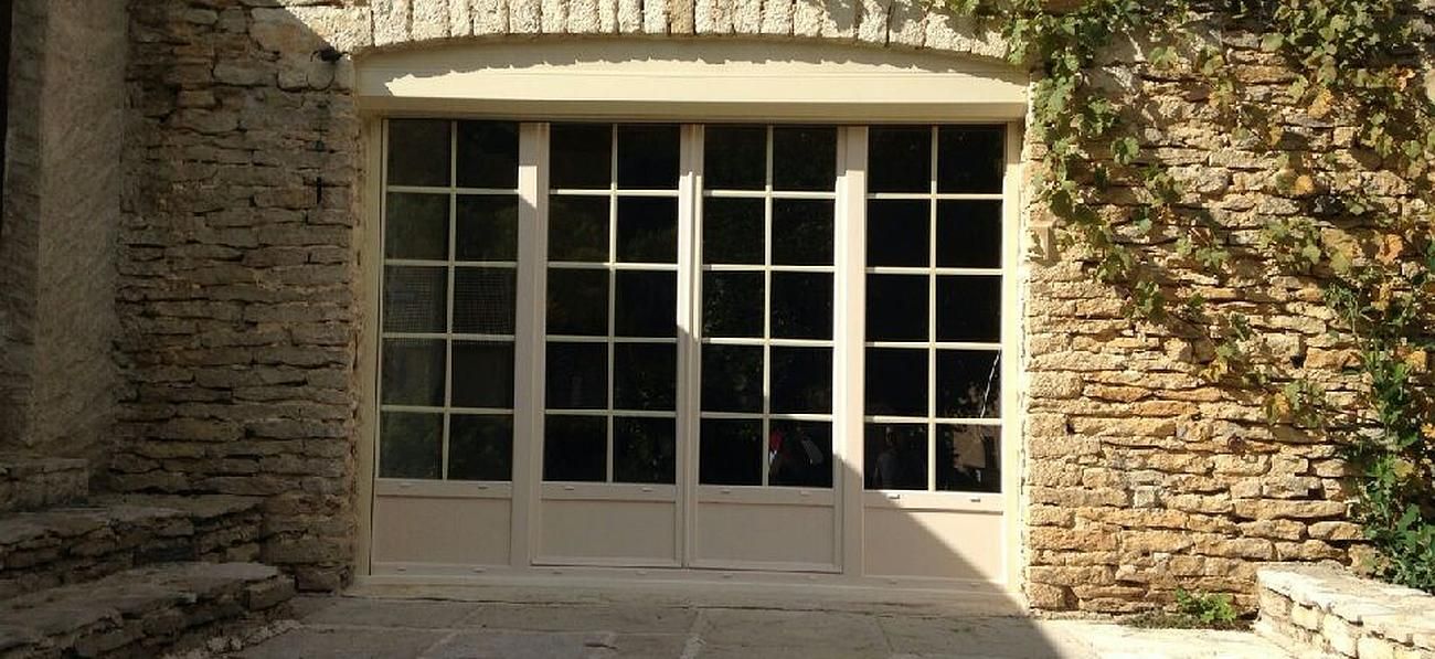 Baie vitrée blanche avec croisillons installée sur une maison en pierre