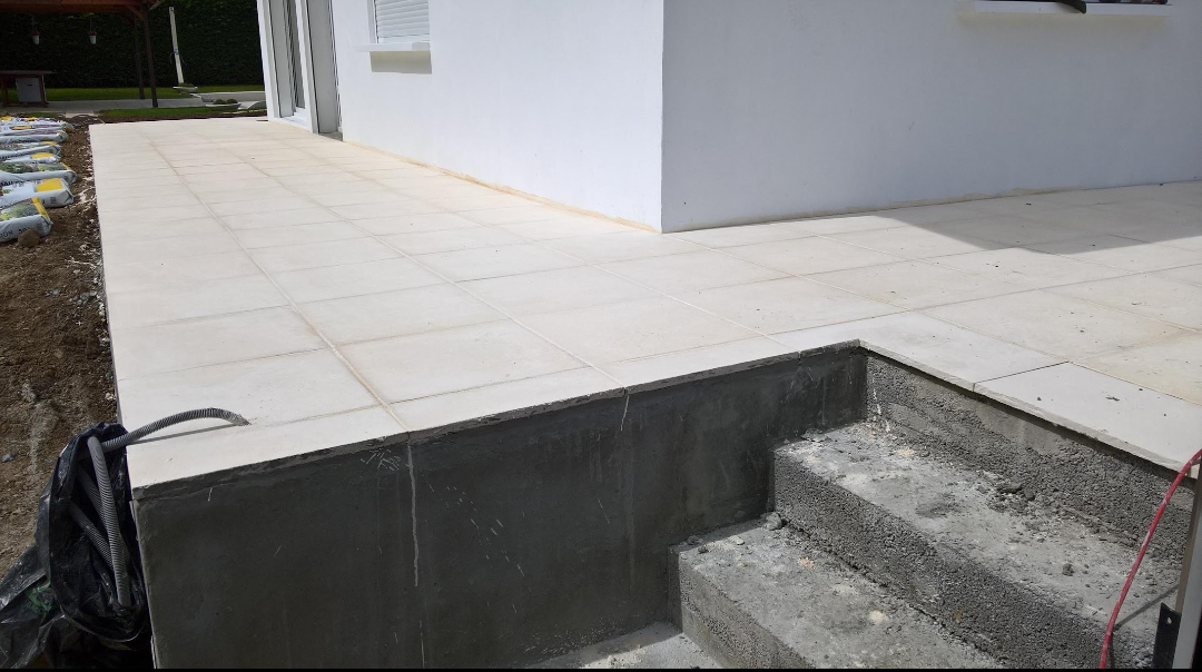 Un patio en béton avec des carreaux de couleur claire, des escaliers et un mur de bâtiment blanc.