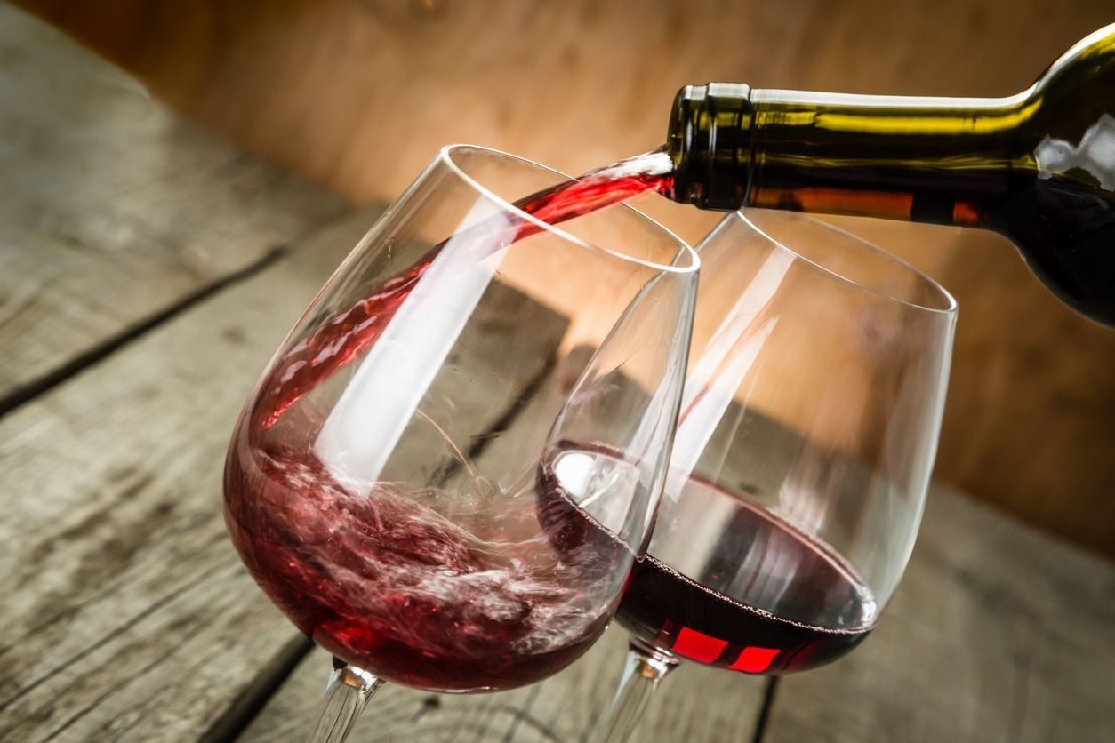 Se vierten dos copas de vino tinto de una botella sobre una mesa de madera.