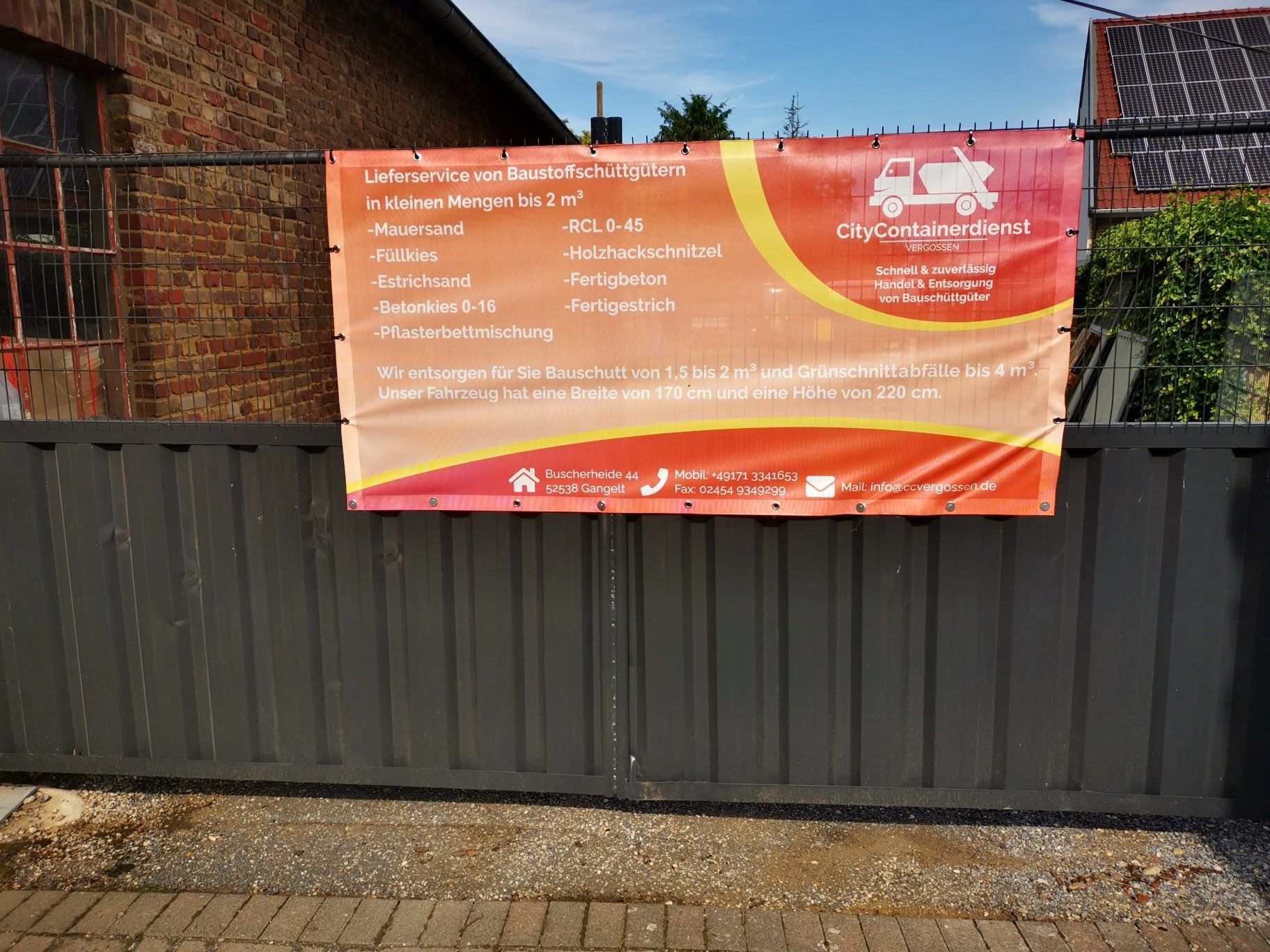 An einem Zaun vor einem Backsteingebäude hängt ein Banner.