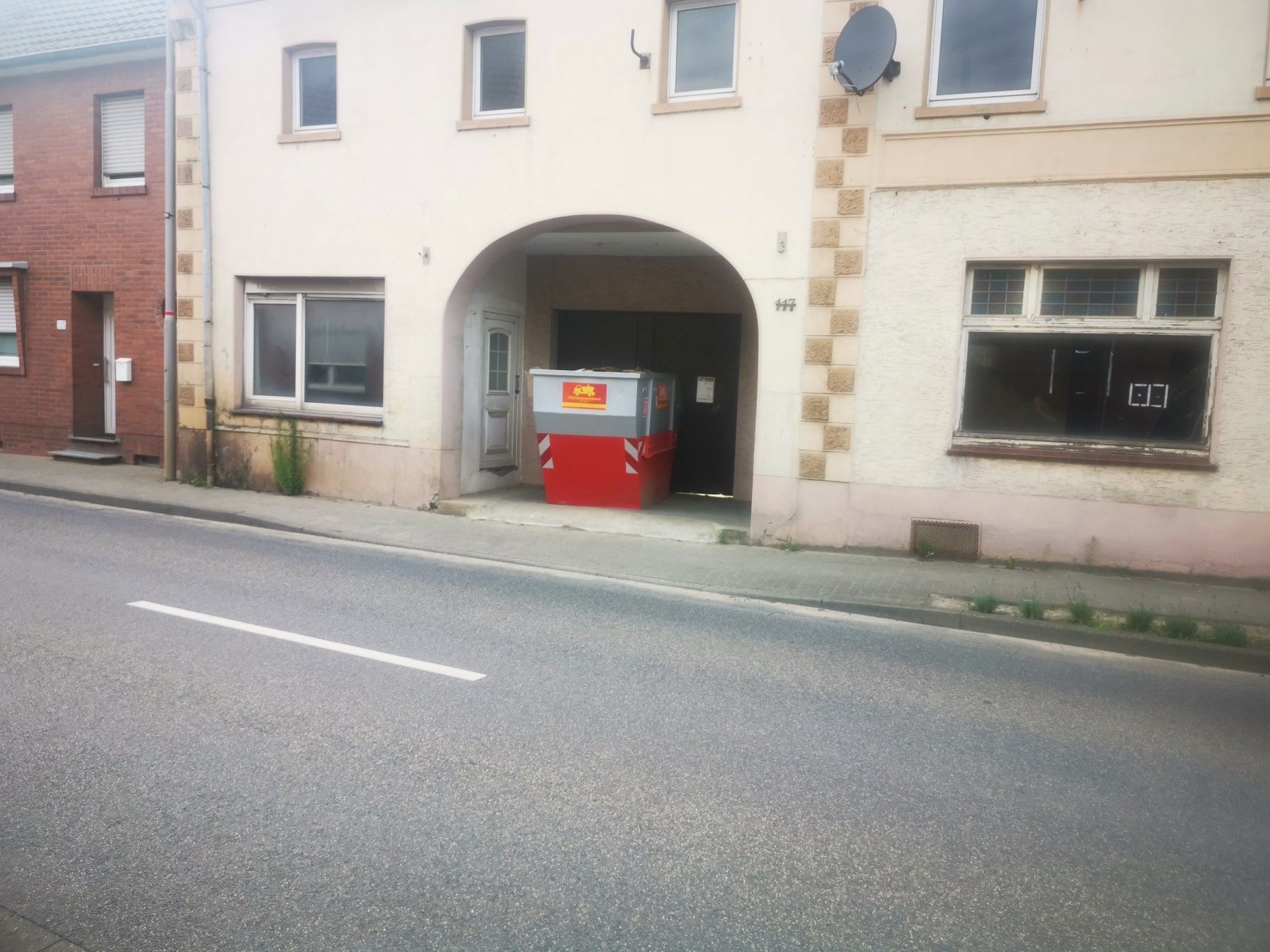 Ein weißes Gebäude mit einem roten Müllcontainer davor