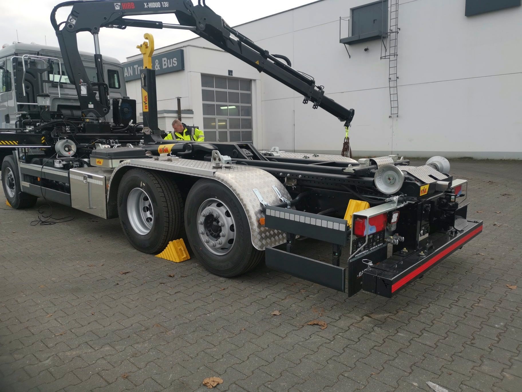 Auf einem Parkplatz steht ein Muldenkipper mit einem daran befestigten Kran.