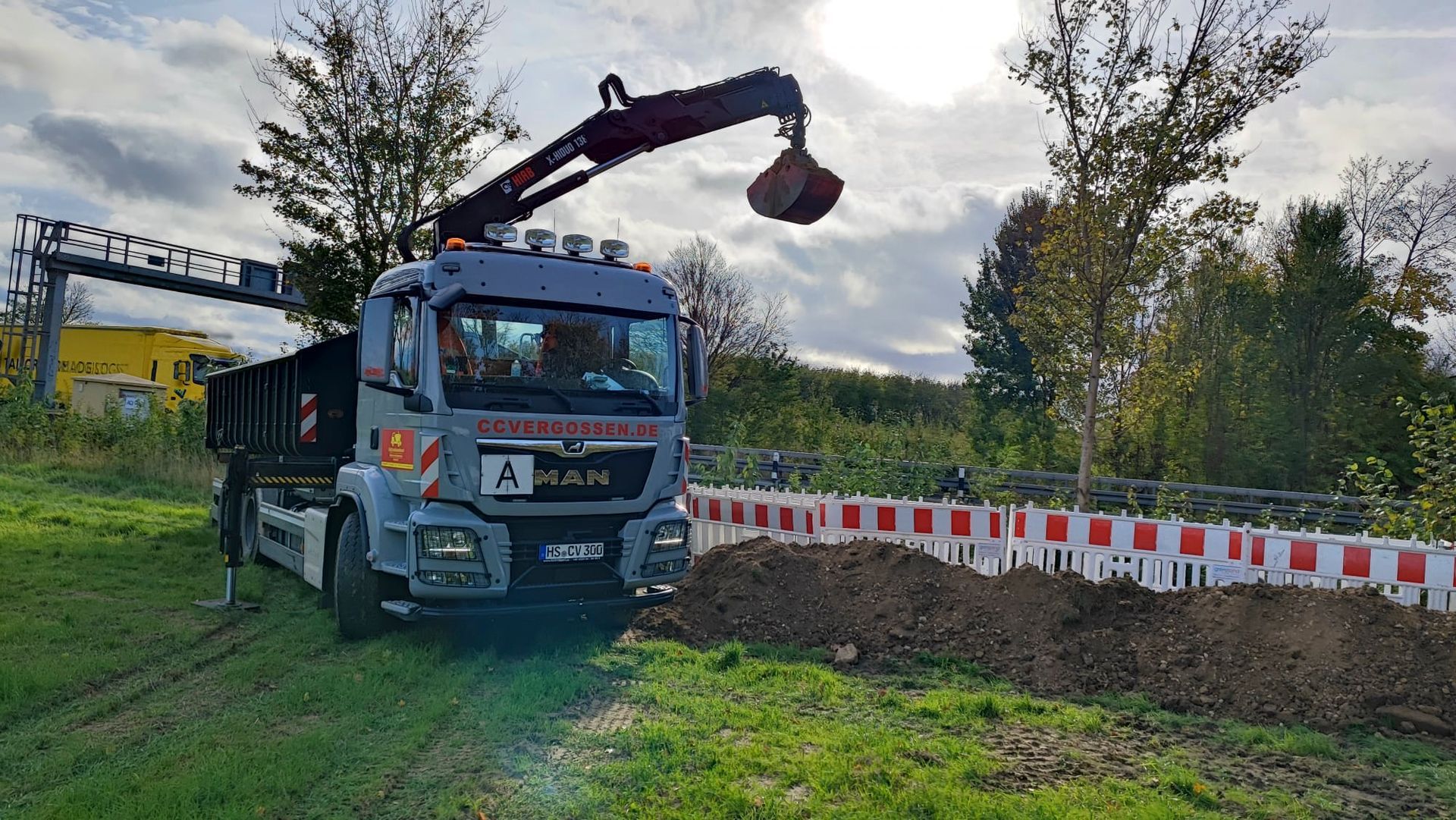 Ein Muldenkipper mit einem daran befestigten Kran steht auf einer Wiese.