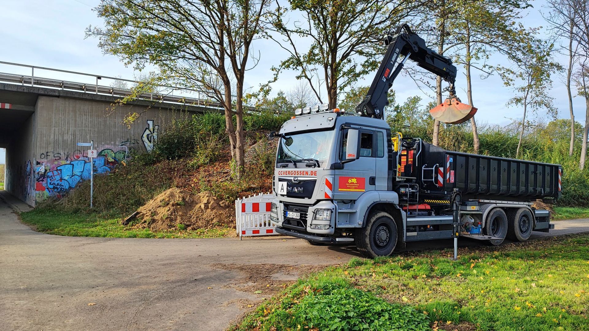 Ein Muldenkipper parkt am Straßenrand neben einer Brücke.