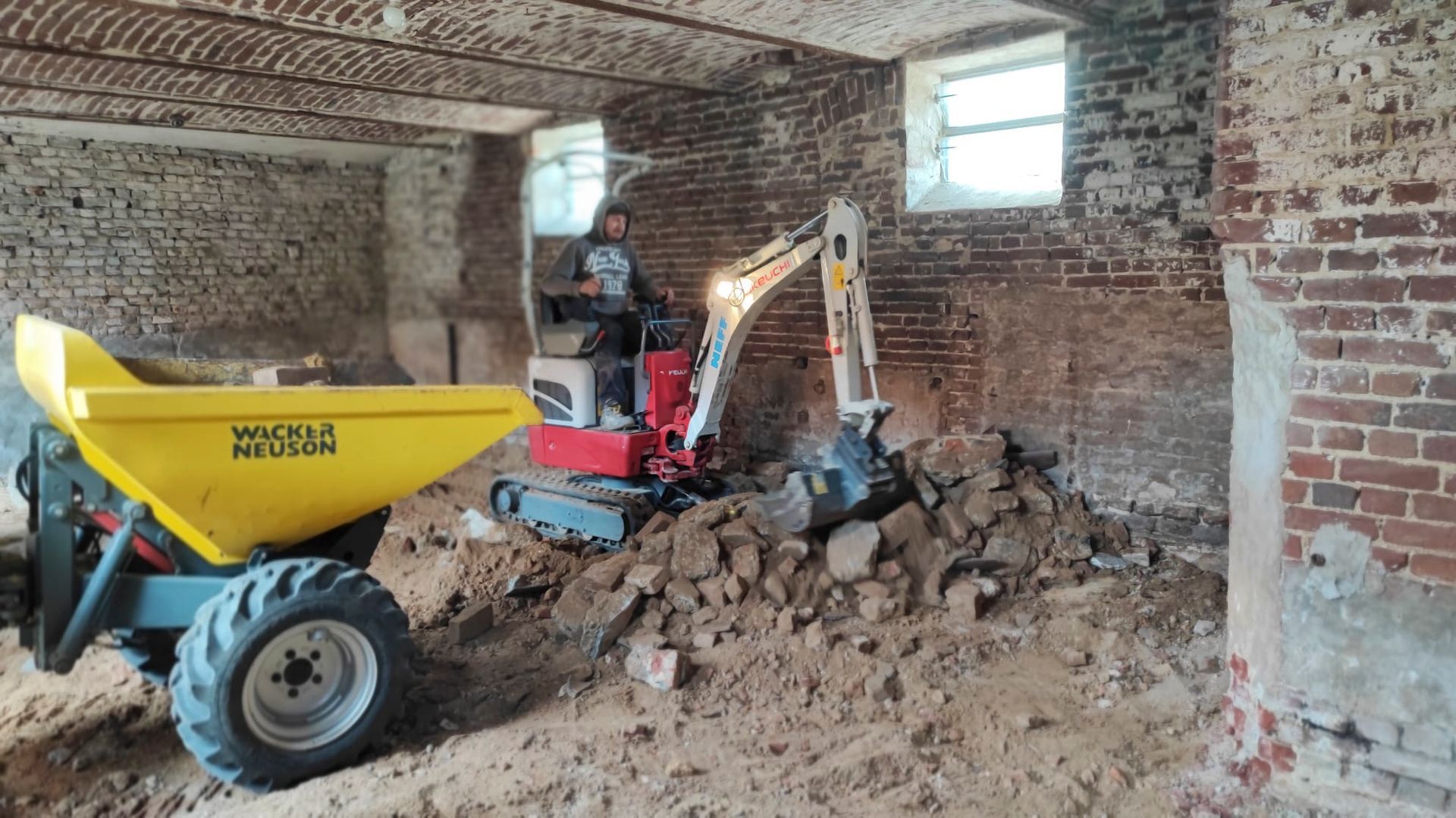 Ein Mann fährt einen Muldenkipper und einen Bagger in einem Backsteingebäude.