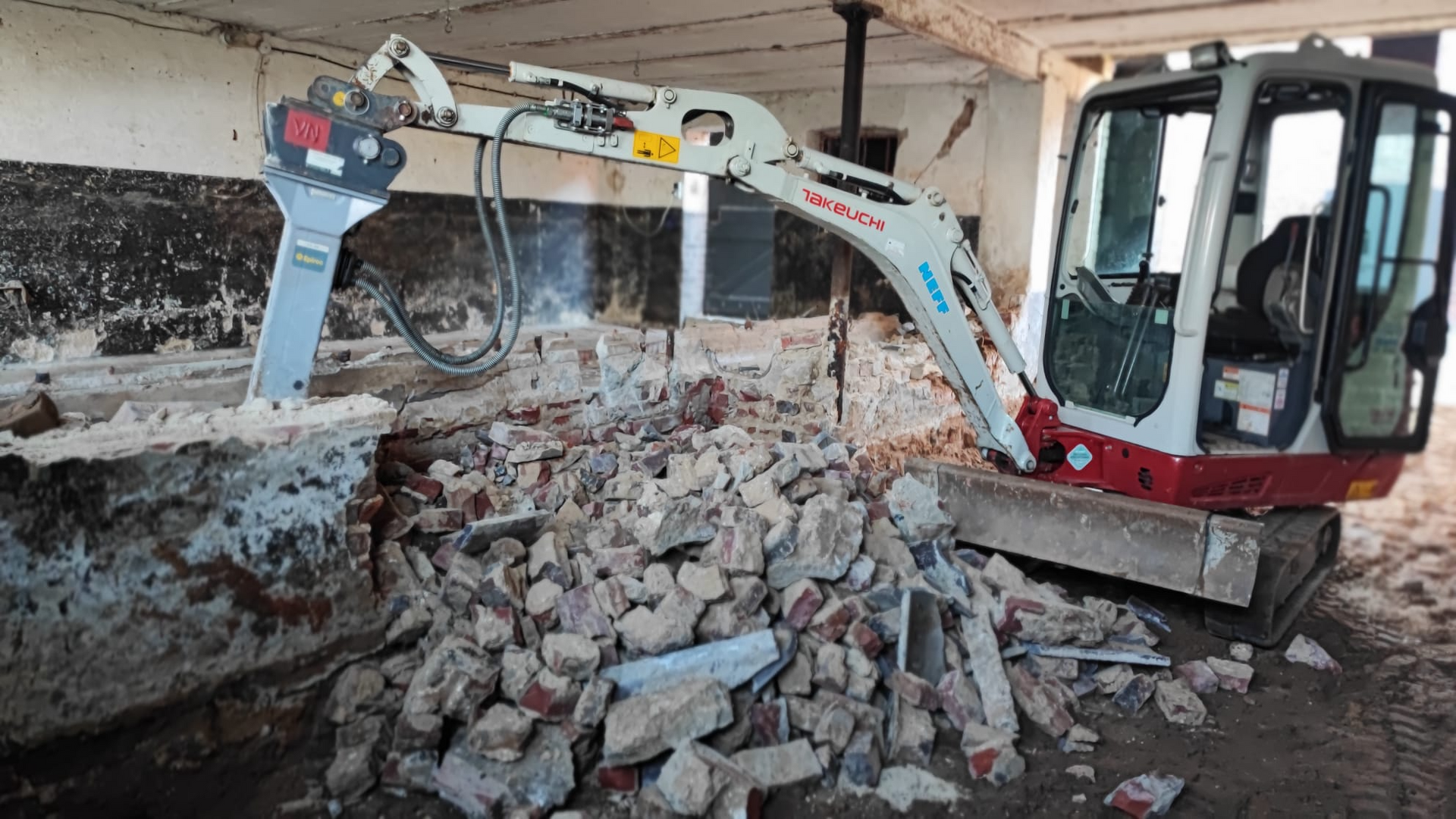 Ein kleiner Bagger bricht eine Ziegelmauer auf.