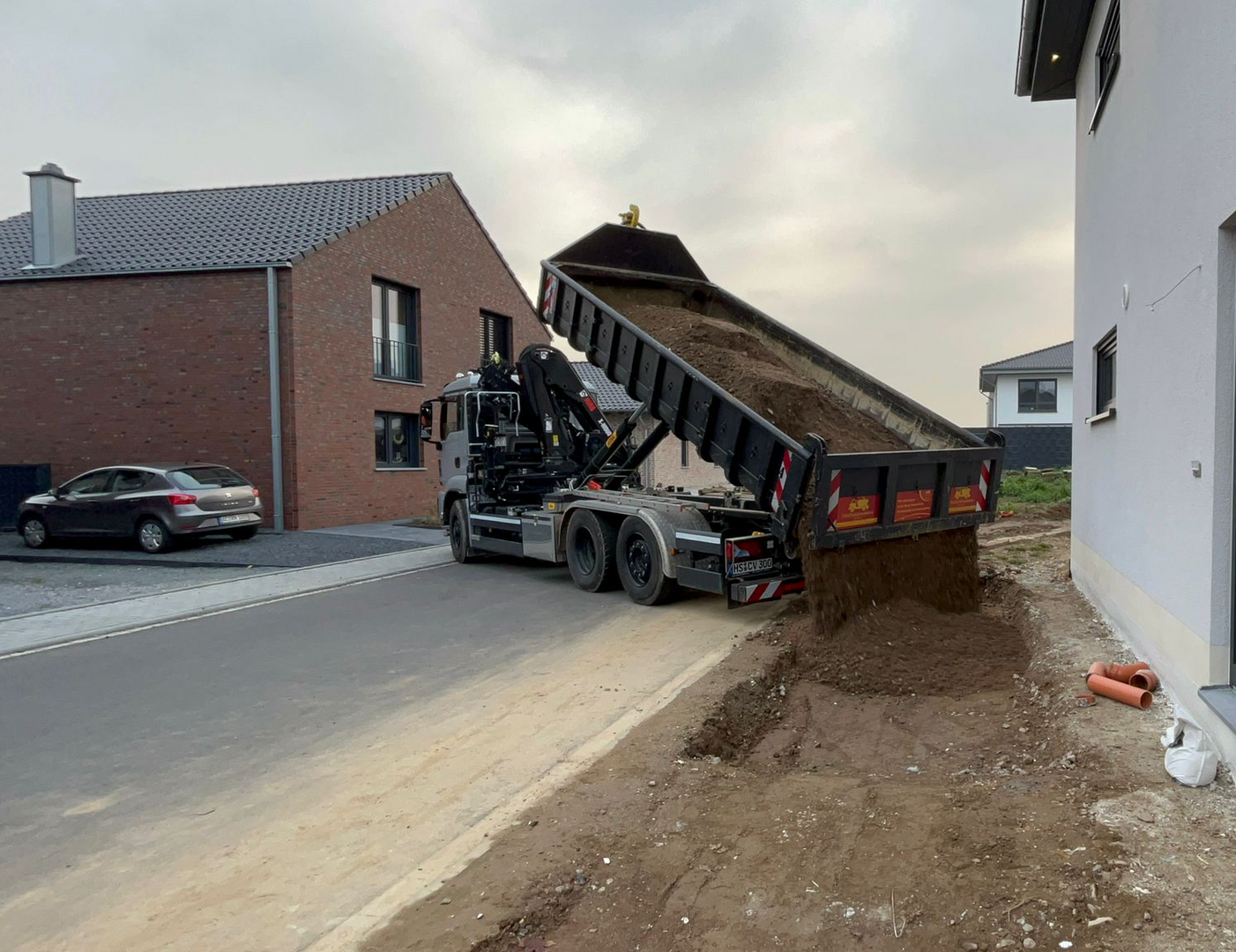 Ein Muldenkipper kippt Erde am Straßenrand ab.