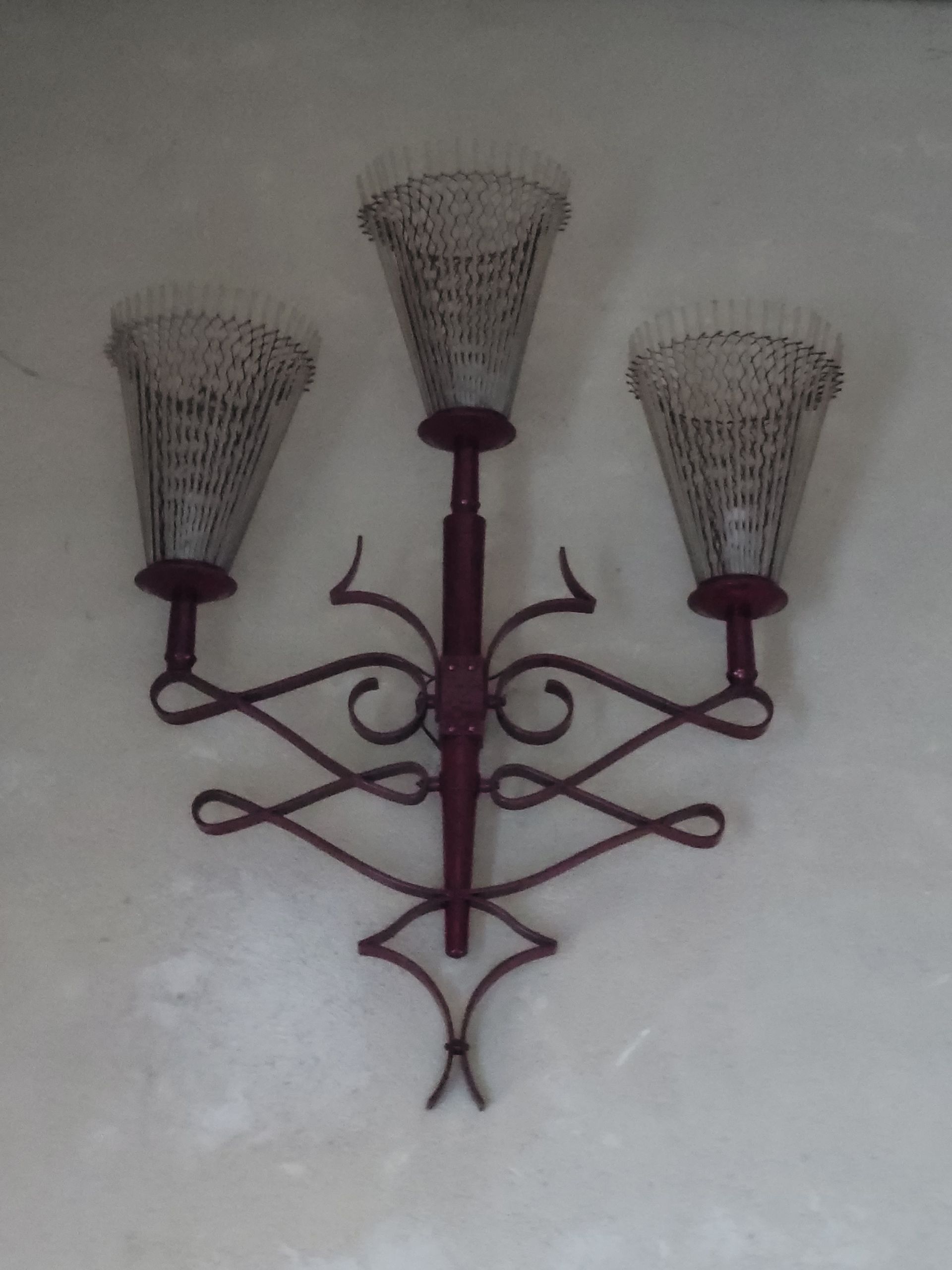 Une applique murale à trois bras avec des volutes en métal brun et trois abat-jour coniques en treillis métallique