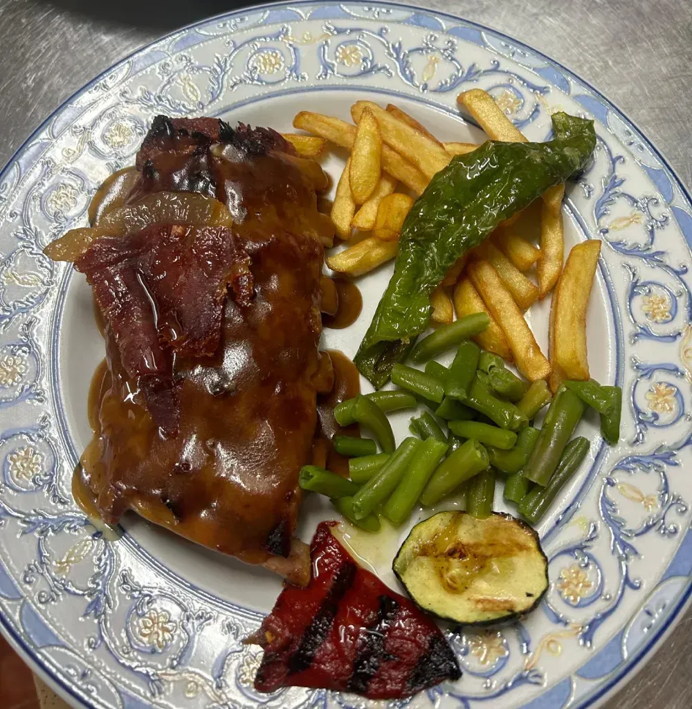 Plato de comida con carne, patatas fritas, judías verdes, pimiento asado, calabacín y salsa.