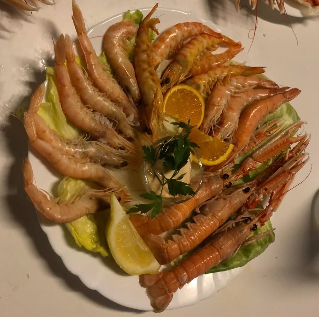 Plato de camarones y langostinos cocidos con rodajas de limón, lechuga y salsa.