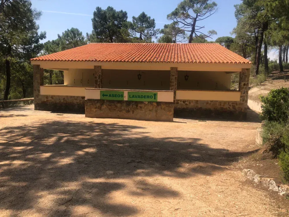 Edificio de baños públicos con techo de tejas en un bosque. Letreros en español sobre la entrada.