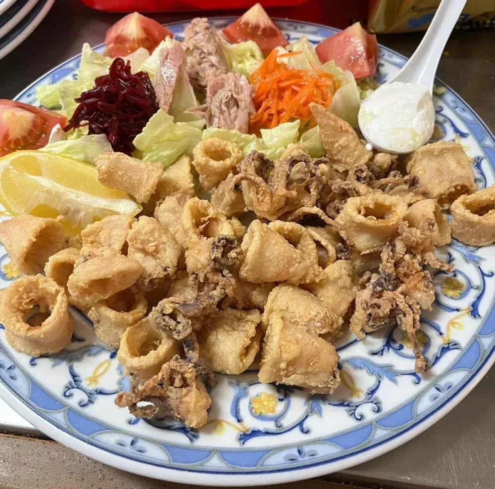 Calamares fritos y ensalada en plato estampado, con rodaja de limón y salsa para mojar.
