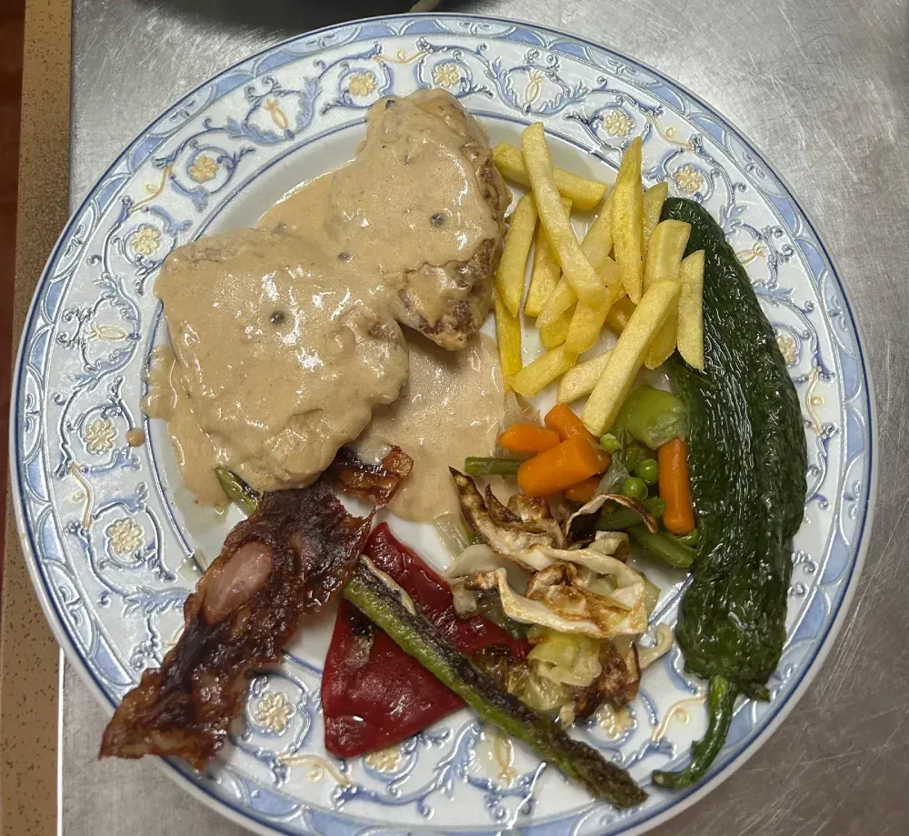 Plato de comida: carne con salsa, patatas fritas, verduras.