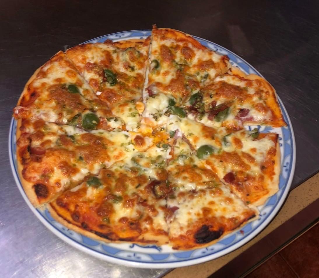 Pizza con queso derretido, pimientos verdes y salsa en un plato con borde azul.