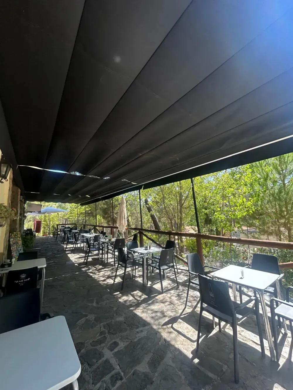 Patio restaurante al aire libre con mesas y sillas bajo un toldo retráctil negro.