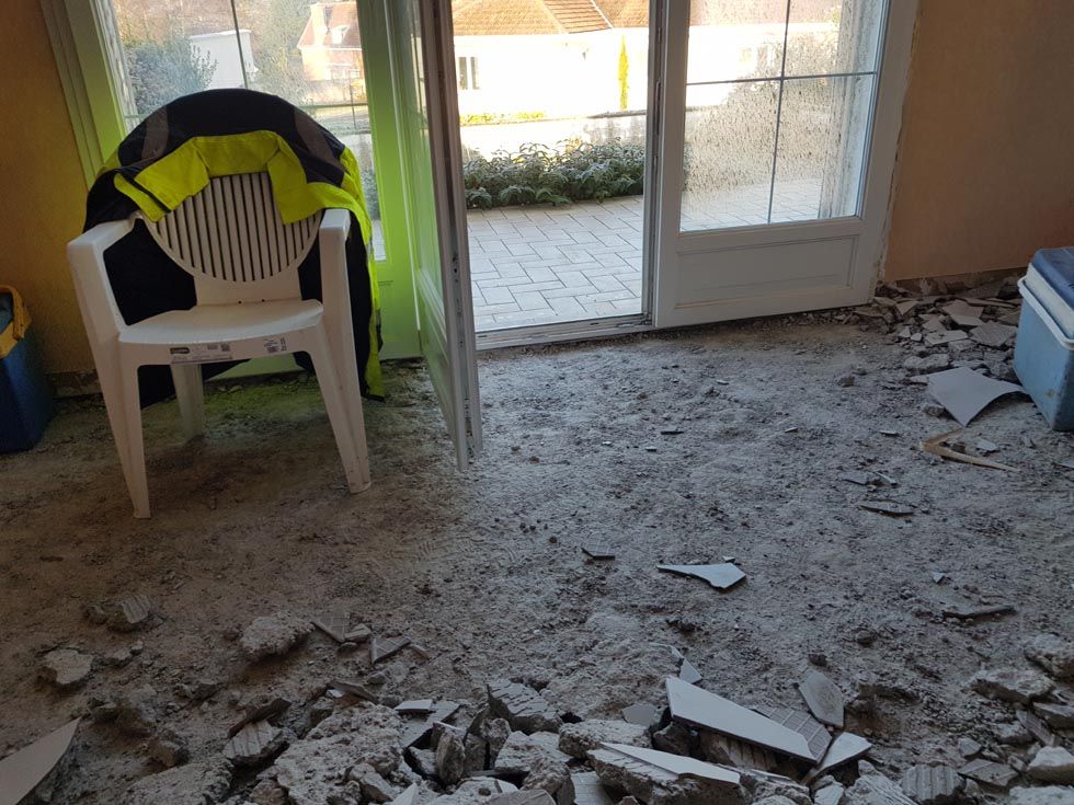 Pièce avec des débris au sol, porte ouverte donnant sur le patio, chaise blanche avec veste.