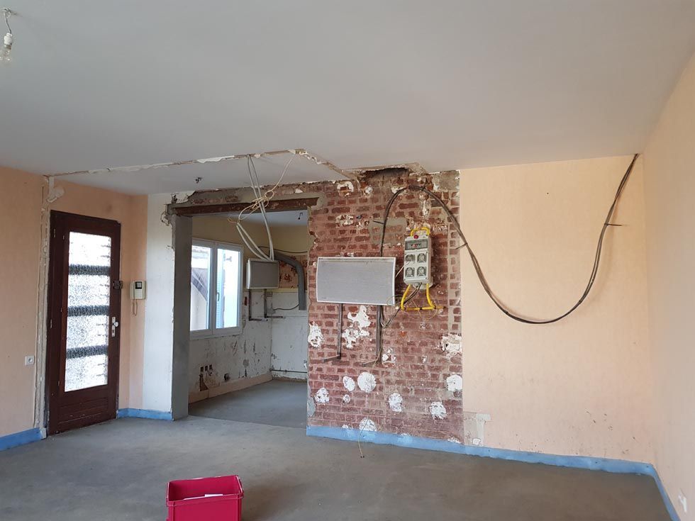 Rénovation intérieure en cours : mur de briques apparentes avec câblage électrique, porte et murs non finis ; pièce vide.