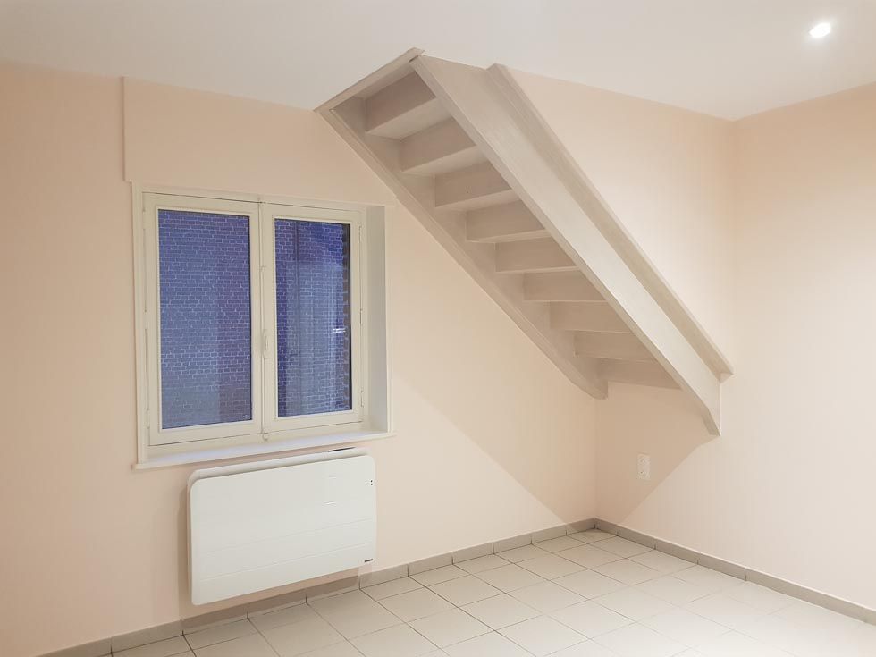 Pièce intérieure avec escalier en angle, fenêtre et radiateur mural.