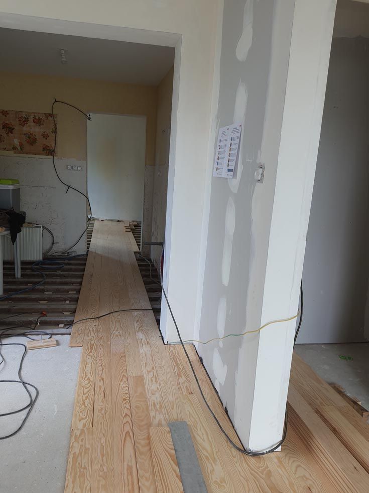 Pose de parquet en cours, câbles électriques en cours de passage. Pilier en plaques de plâtre et encadrement de porte visibles.
