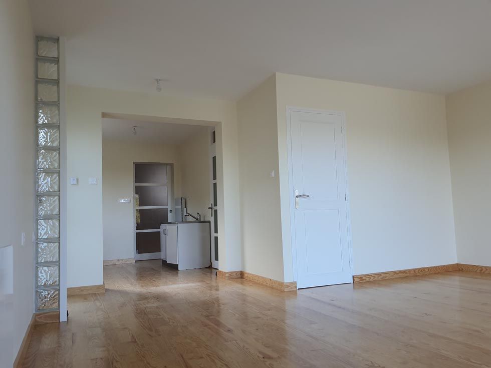 Pièce vide avec parquet, murs clairs, colonne en pavés de verre, porte et porte blanche.