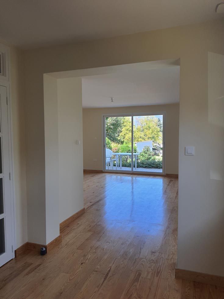 Vue intérieure d'une pièce avec parquet, porte et balcon donnant sur de la verdure.