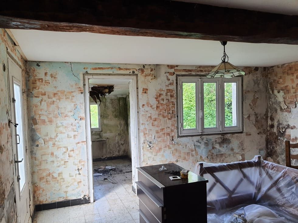 Intérieur d'une pièce délabrée avec peinture écaillée, porte ouverte, fenêtre et meubles en bois sombre.