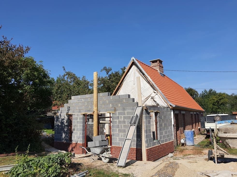 Construction d'un bâtiment en briques et parpaings. Une échelle est appuyée contre le mur sous un ciel bleu.