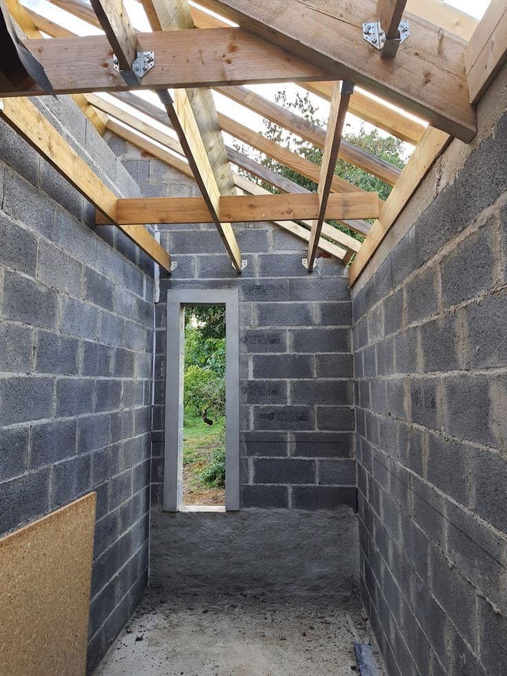 Intérieur d'un bâtiment en construction, murs en parpaings gris, poutres de toit en bois, petite fenêtre, non peint.