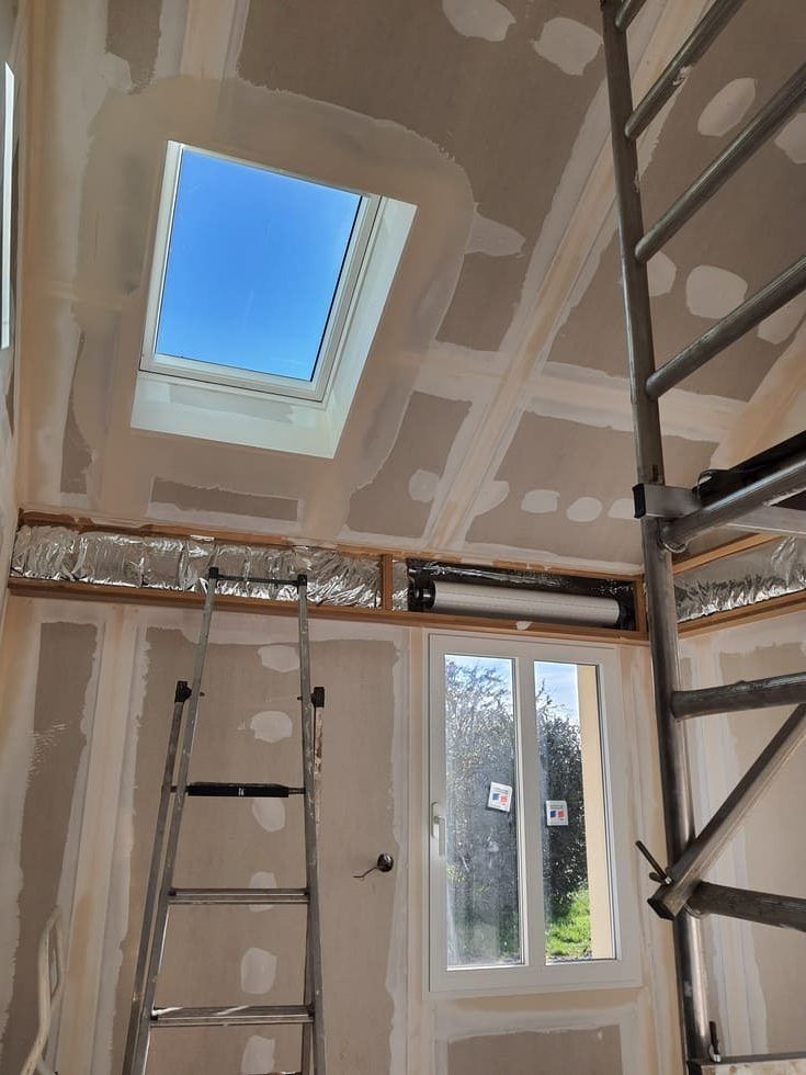 Intérieur avec cloisons sèches, puits de lumière, fenêtre, échelle, échafaudage et isolation apparente.