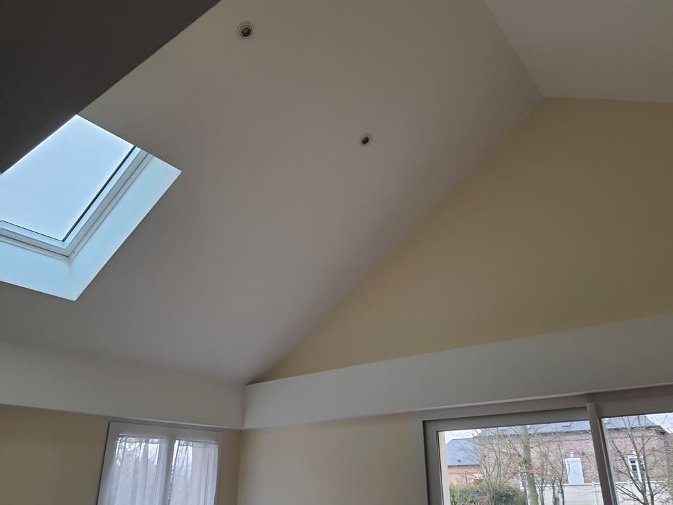 Pièce intérieure avec puits de lumière et plafond mansardé ; murs crème et jaune clair.
