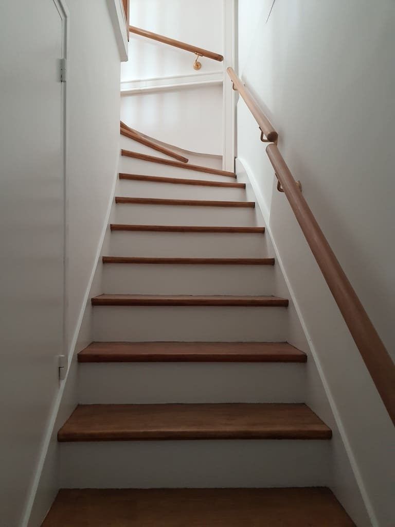 Escalier avec marches et rampes en bois menant vers le haut, contre des murs blancs.