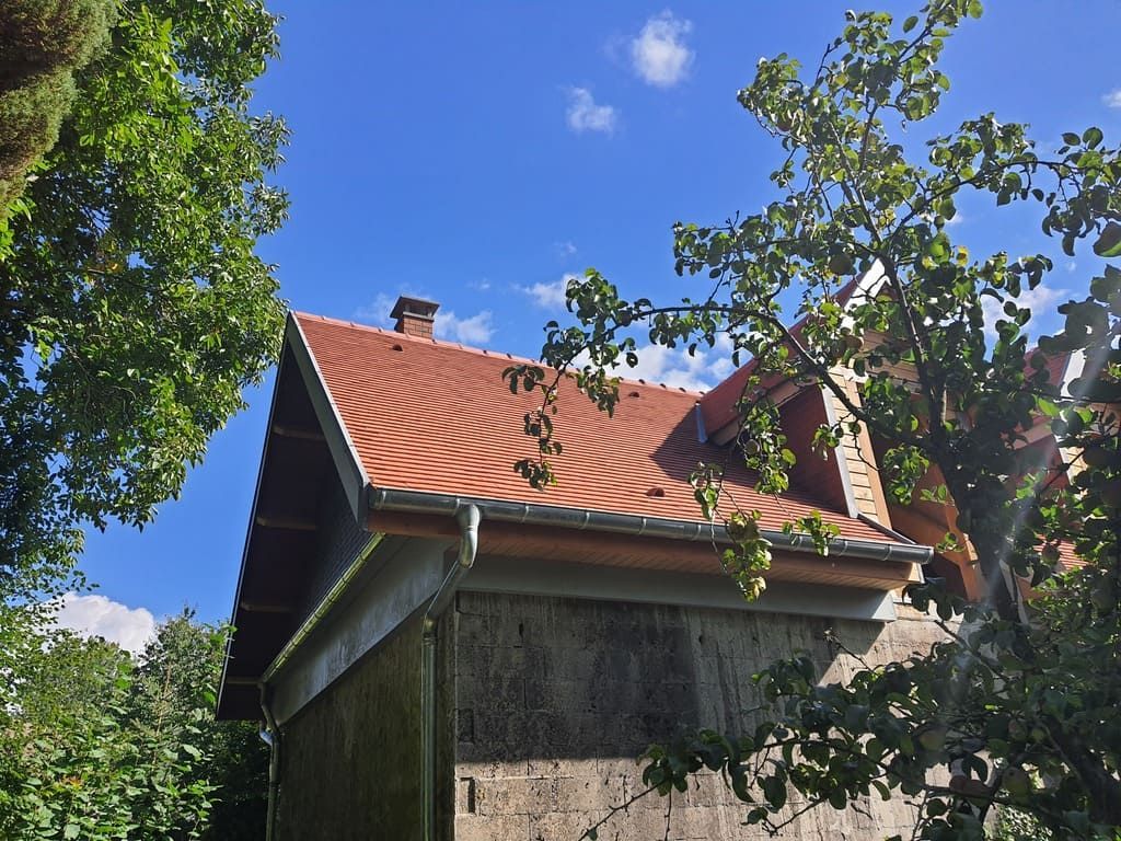 Un bâtiment au toit rouge se détachant sur un ciel bleu, encadré par des arbres verts.