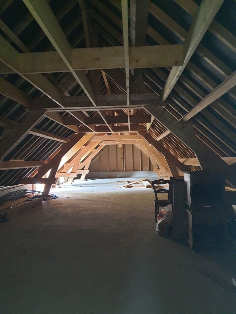 Intérieur de combles en bois, charpente apparente, lumière naturelle illuminant l'espace.
