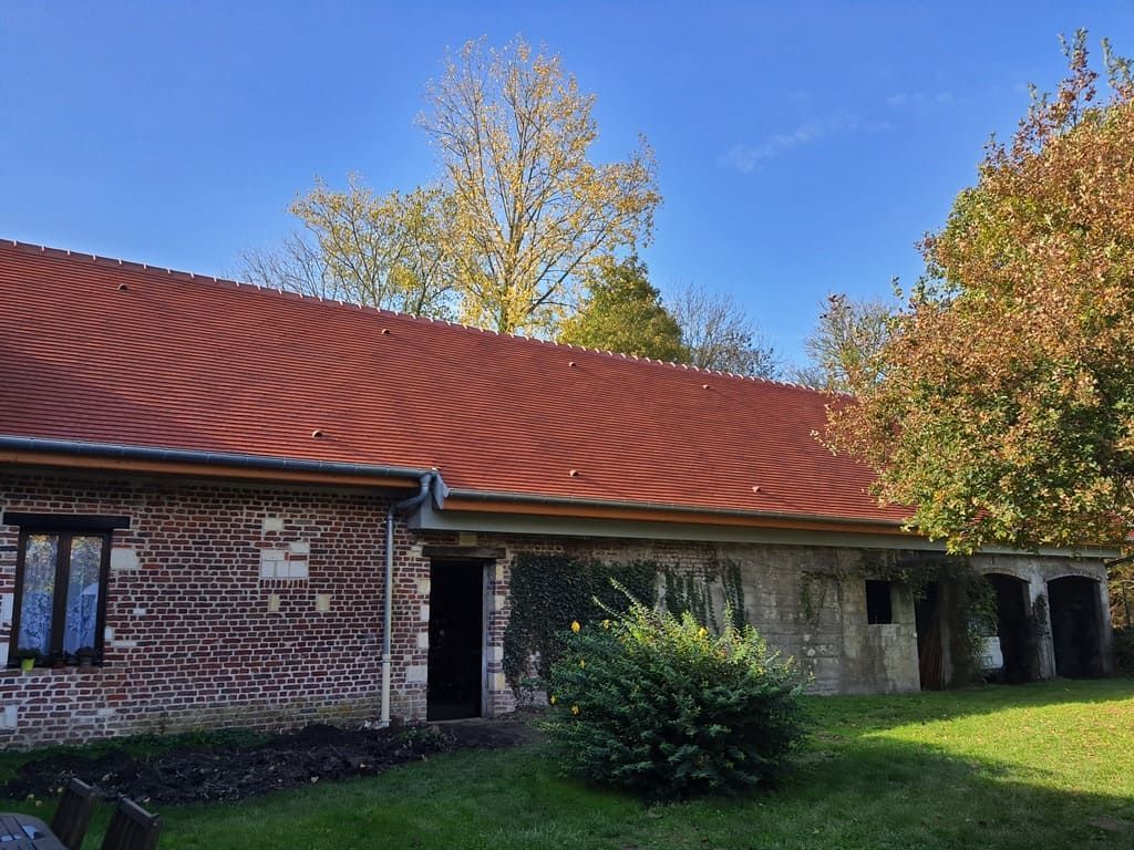 Bâtiment en briques avec un toit en tôle ondulée rouge et des arbres par une journée ensoleillée.
