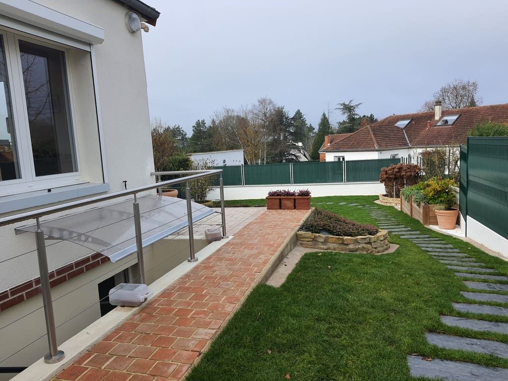 Extérieur d'une maison avec allée en briques et pelouse verte. Garde-corps en acier inoxydable avec panneaux transparents.