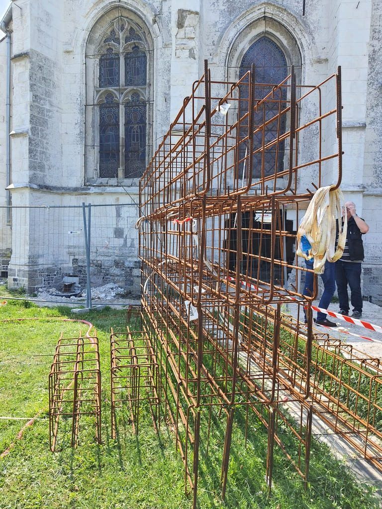 Échafaudage métallique rouillé près d'une église ; deux personnes se tiennent à proximité.