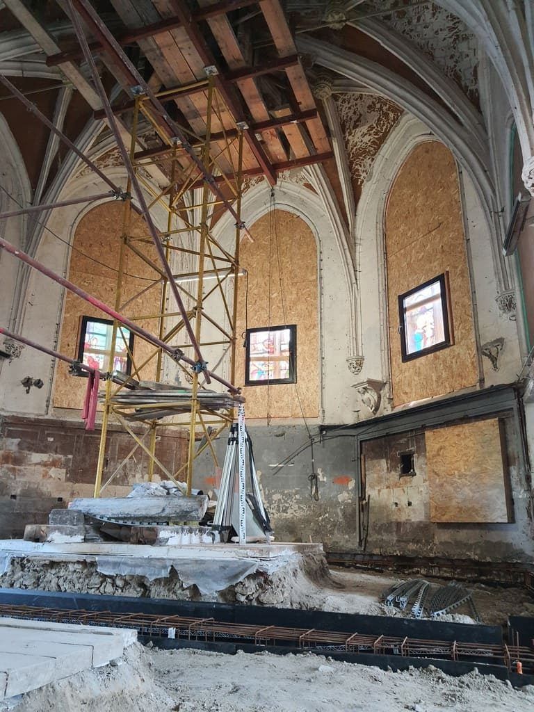 Vue intérieure d'un bâtiment en rénovation, avec des échafaudages, des murs apparents et des fenêtres condamnées.