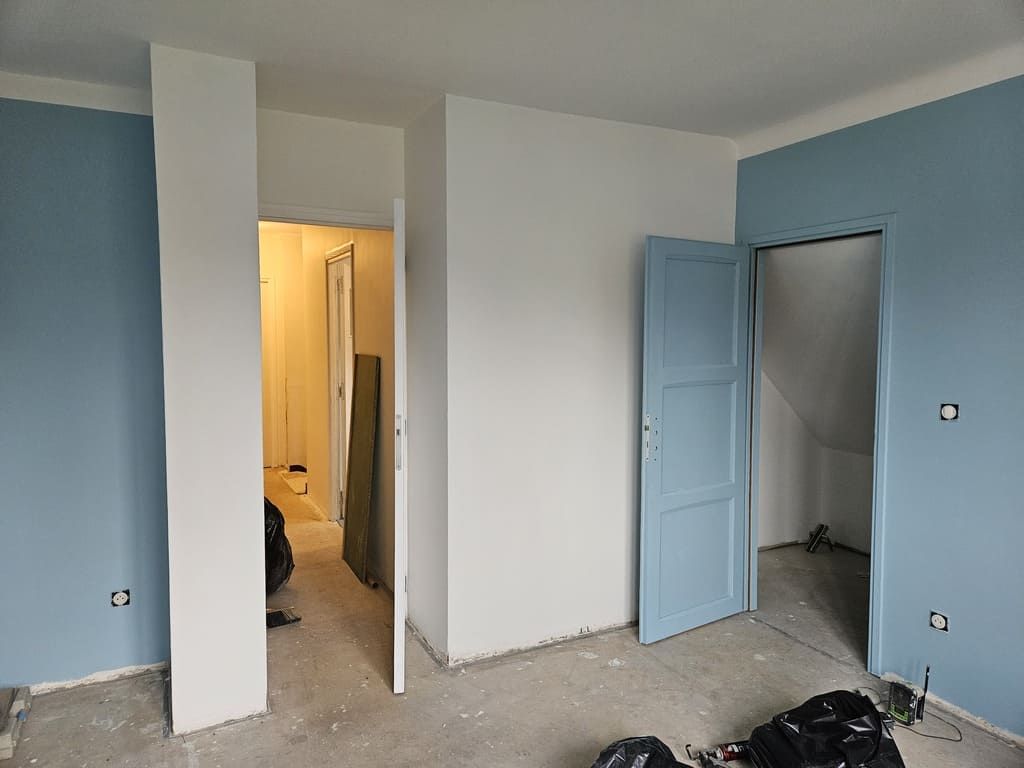 Pièce aux murs bleus et blancs, deux portes ouvertes et sol en béton apparent.