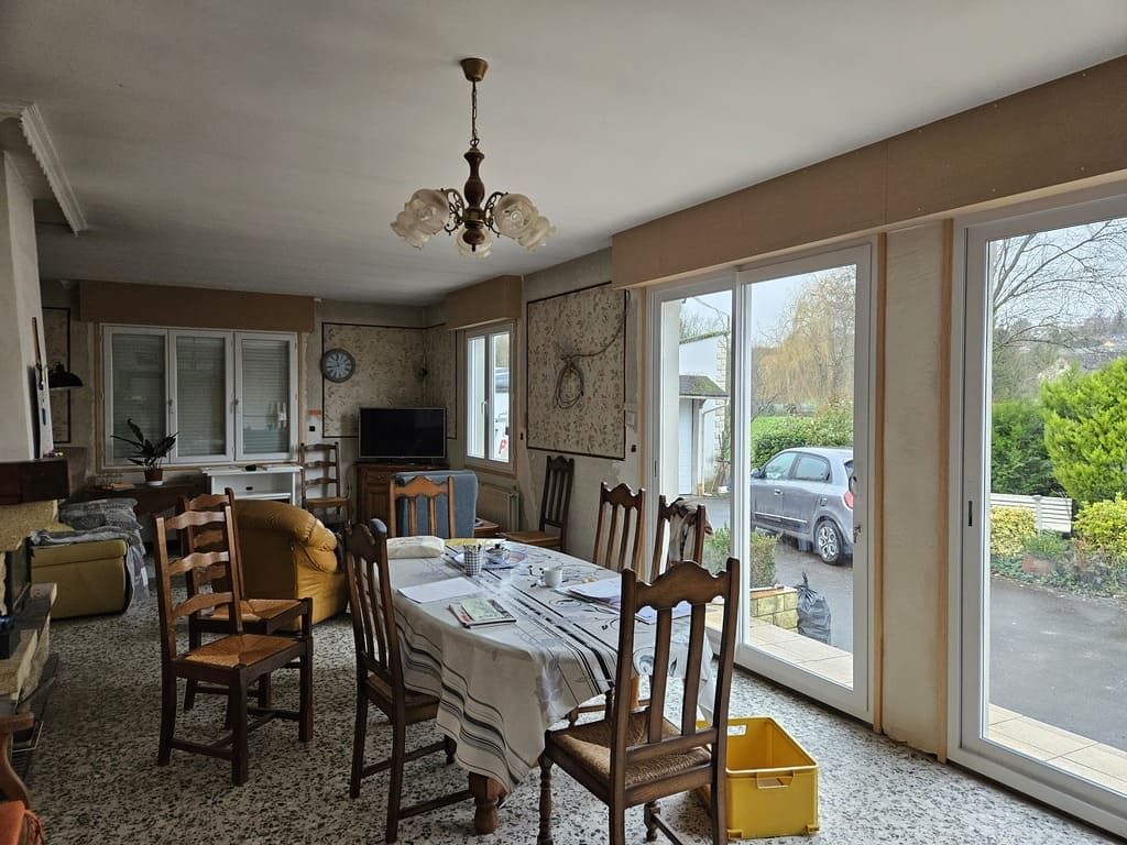 Salle à manger avec table dressée, chaises et grandes fenêtres donnant sur une cour.