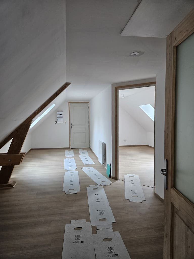 Vue intérieure d'un couloir mansardé avec un nouveau revêtement de sol et des portes ouvertes donnant sur d'autres pièces ; construction partiellement achevée.