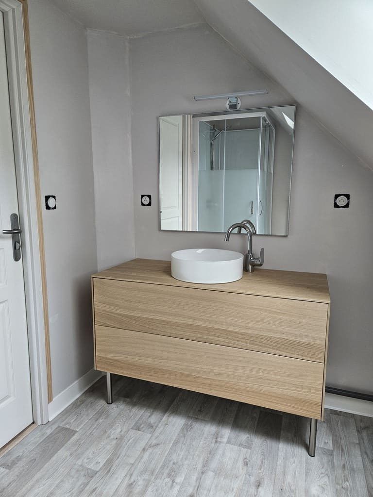 Salle de bains avec meuble-lavabo en bois, lavabo blanc et miroir sur un mur gris.