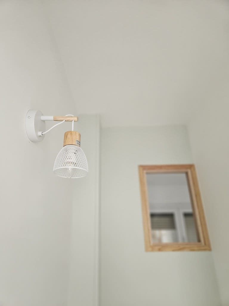 Mur blanc avec une applique murale blanche et boisée et un miroir encadré.