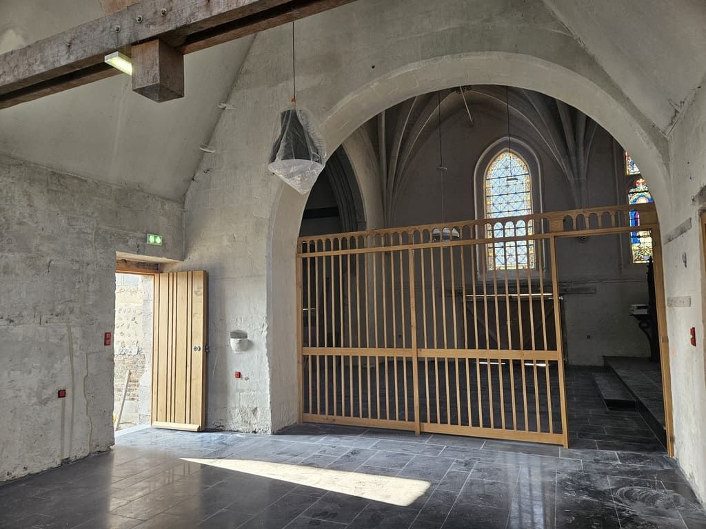 Intérieur d'un bâtiment en pierre avec des structures en bois, une porte et une fenêtre cintrée.