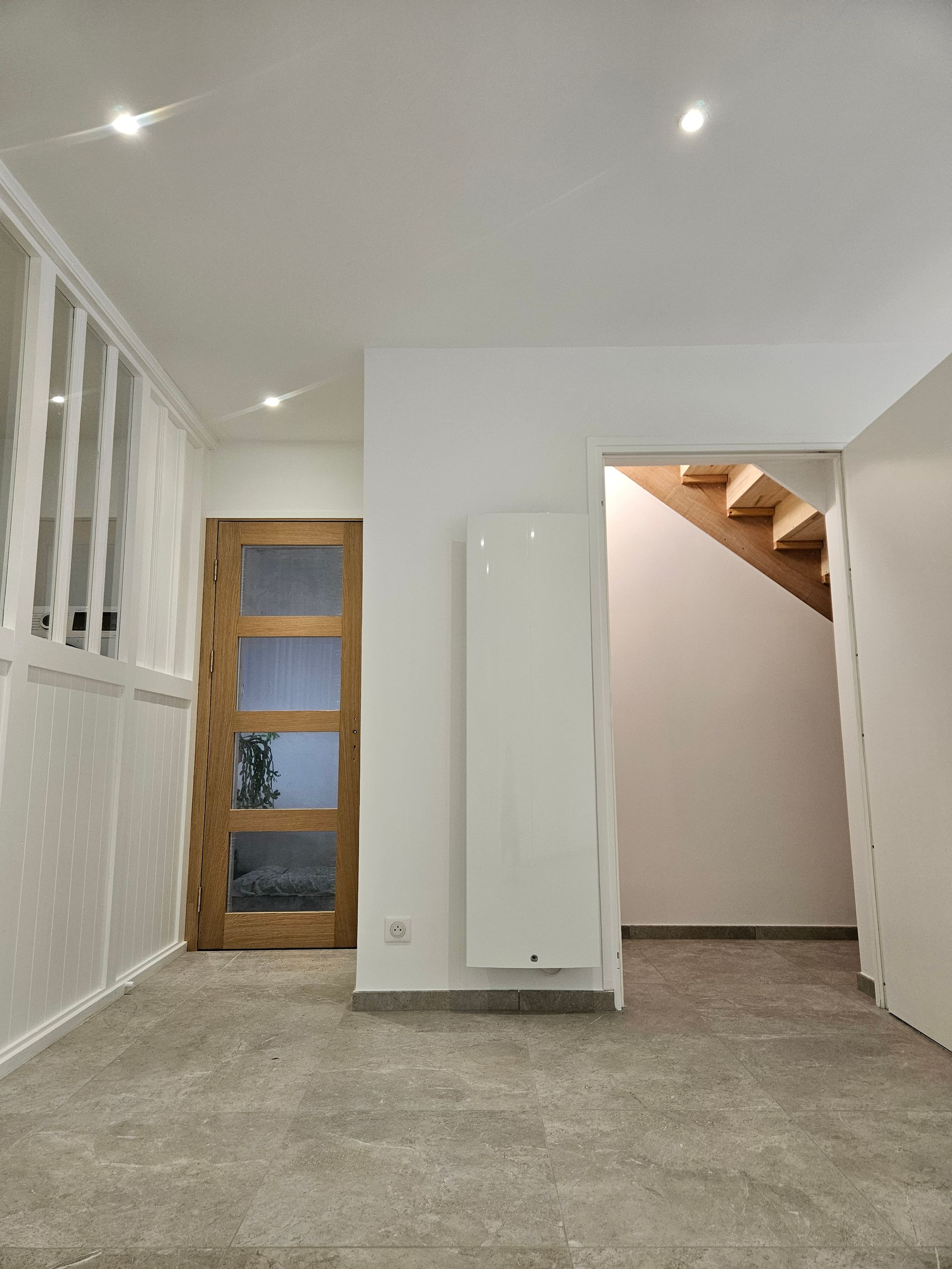 Pièce blanche vide avec sol carrelé, porte en bois et escalier