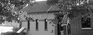 Photo en noir et blanc d'un bâtiment portant l'enseigne MAIRIE. Des arbres encadrent le bâtiment, qui possède un toit de tuiles et de petites fenêtres.