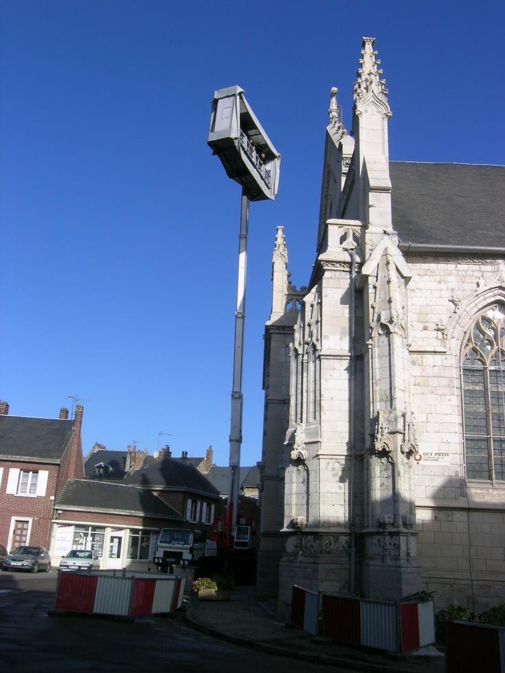 Un ascenseur imposant, avec une plateforme s'étendant très haut à côté d'une église en pierre, par une journée ensoleillée.