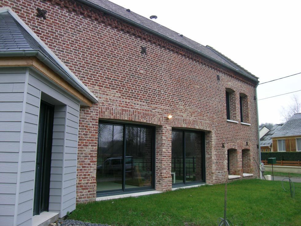 Bâtiment en briques avec de grandes fenêtres à cadre noir et une structure aux murs gris, dans une cour gazonnée.